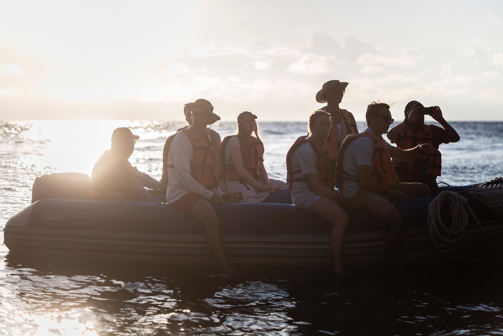 Group of people wearing life jackets on a boat at sunset, with one person taking a photo over the water.