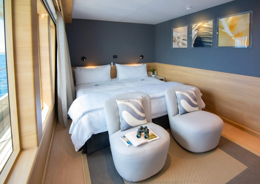 Hotel room with a large bed, two white pillows, and two modern gray chairs at the foot