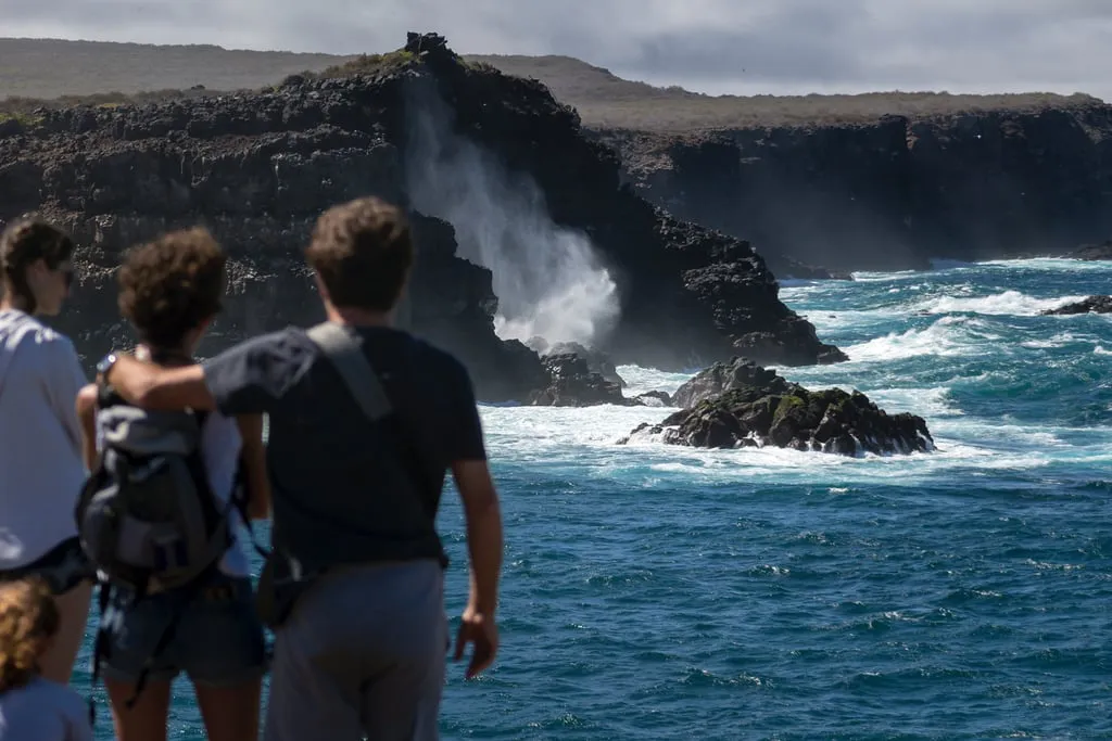 Group of people with backpacks overlook a rugged coastline as turquoise waves crash
