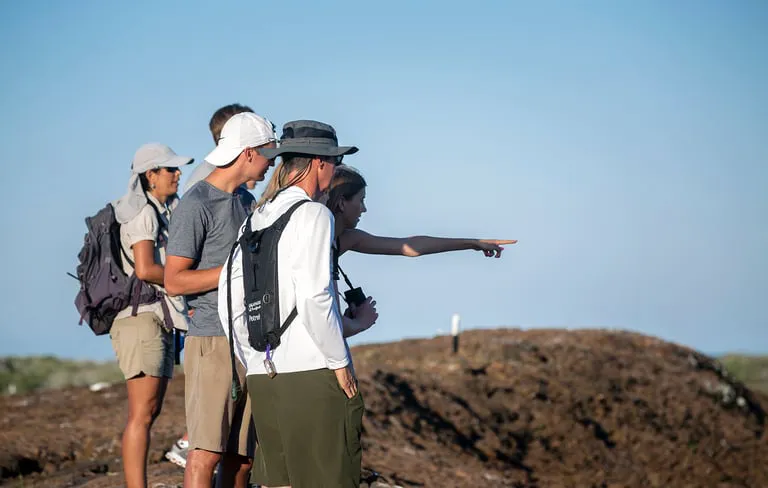 Group of hikers on a rocky coastline, one person points toward something in the distance.