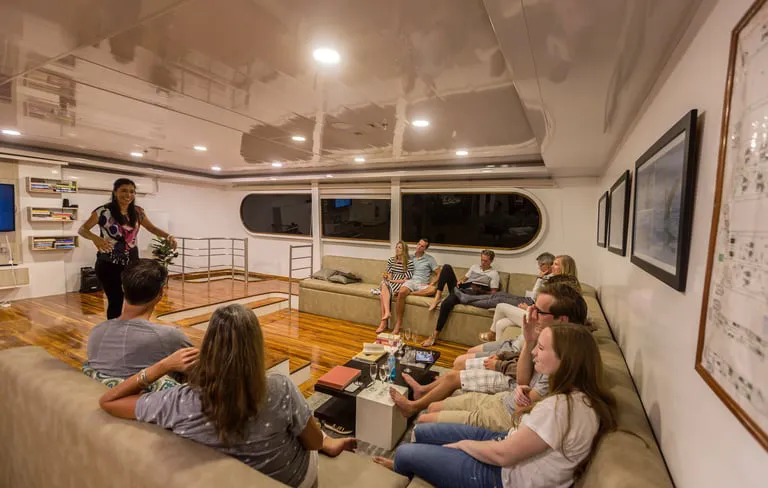 A woman presents to a small group seated on couches in a modern living-room-style lounge.