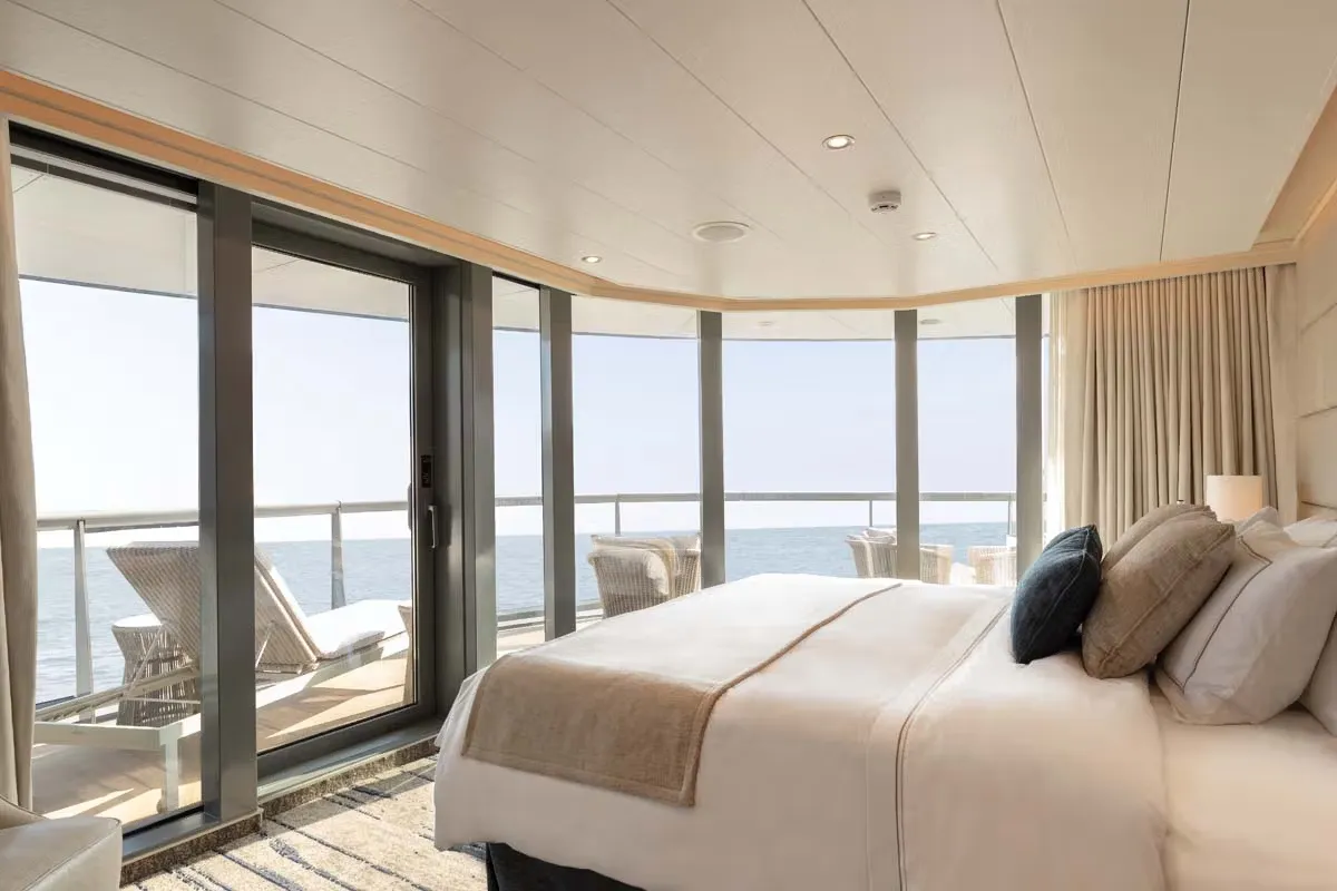 Bright hotel bedroom with a large bed and neutral linens, opening to a balcony