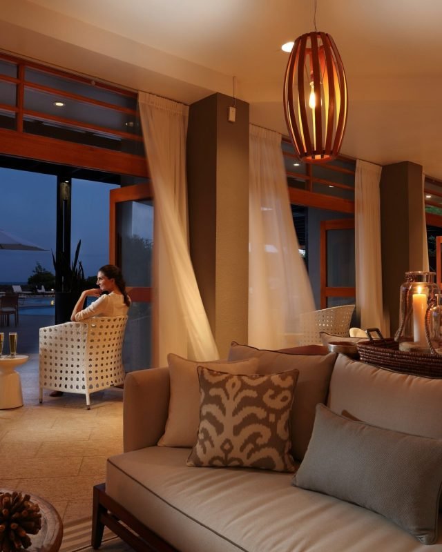 Cozy indoor lounge at dusk with a beige sofa, patterned pillows, and candles on a coffee table